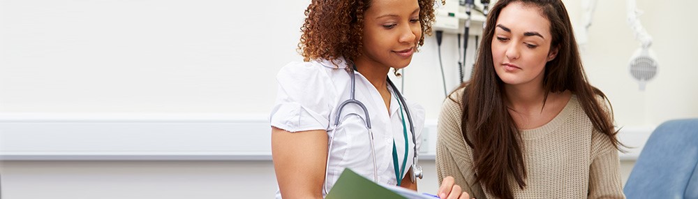 Una enfermera y una paciente leen juntas un folleto médico en una sala de examinación.