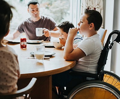 Un niño sentado en una silla de ruedas en una mesa come con su familia.