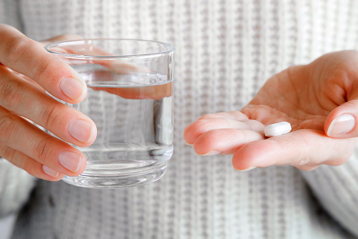 Un acercamiento de las manos de una persona sosteniendo un vaso de agua y una pastilla.