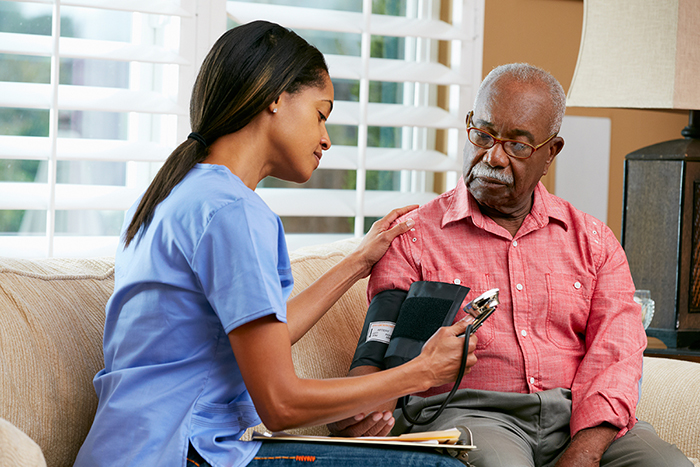Una enfermera toma la presión arterial de un anciano. Ambos son afroamericanos.