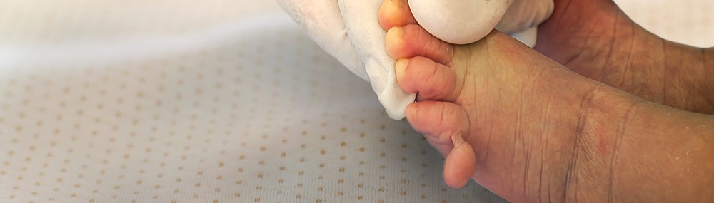 Una mano con un guante de goma sostiene el pie de un bebé recién nacido.