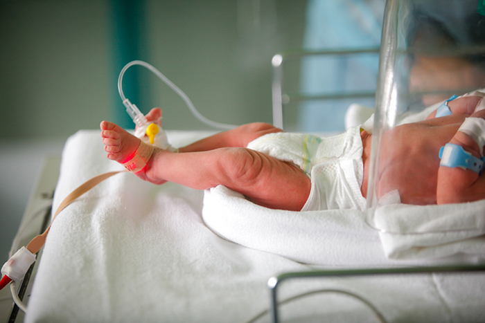 Bebé acostado en la cuna de un hospital con una vía intravenosa en el pie.