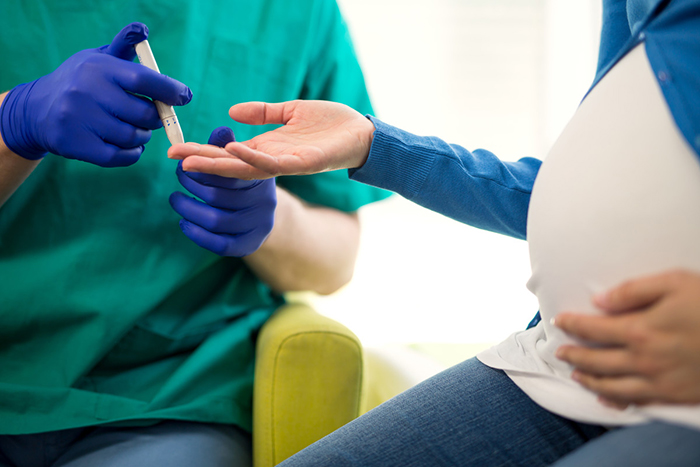 Mujer embarazada que estira el dedo hacia un técnico para que tome una muestra de sangre con un pinchazo.