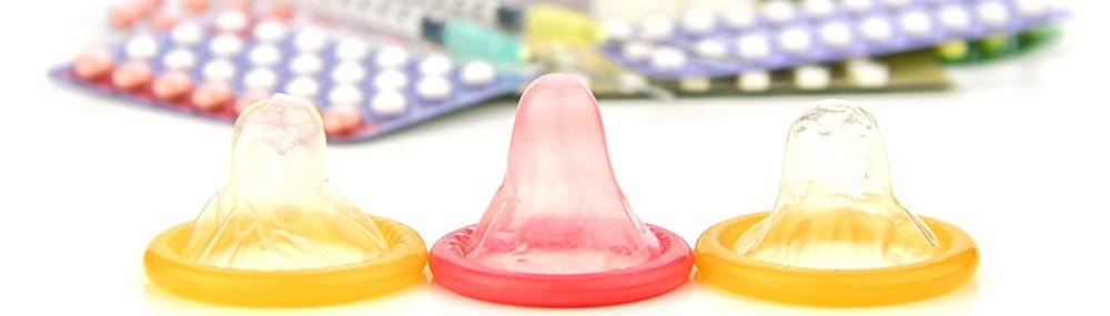 Tres condones con píldoras anticonceptivas y otras formas de anticoncepción en el fondo.
