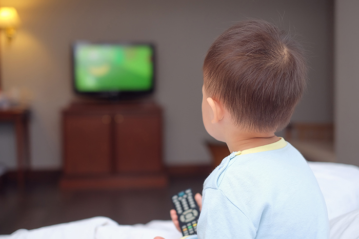 Un niño que sostiene un control remoto de televisión, frente a un televisor.