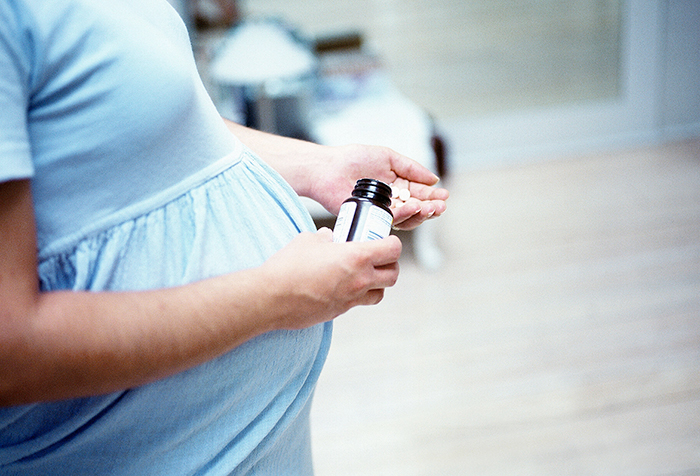 Vista lateral del torso de una mujer embarazada que sostiene una botella de medicina en una mano y pastillas en la otra.