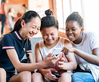 Tres chicas adolescentes se ríen mientras miran uno de sus dispositivos móviles.