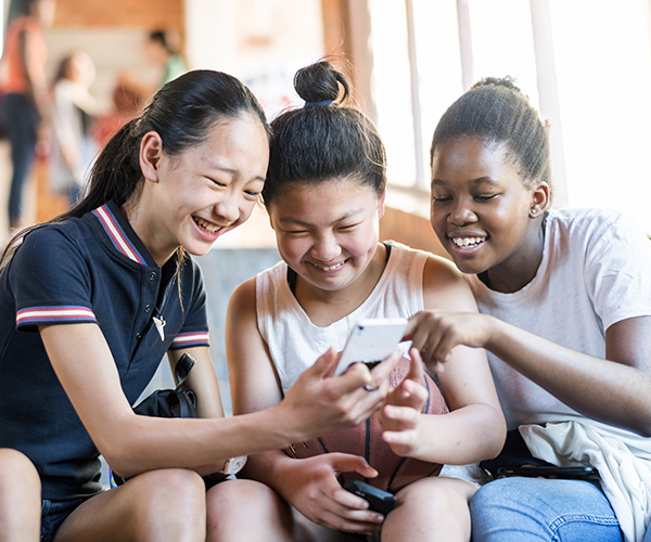 Tres chicas adolescentes se ríen mientras miran uno de sus dispositivos móviles.