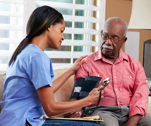 Una enfermera toma la presión sanguínea de un adulto mayor. Ambos son afroamericanos.