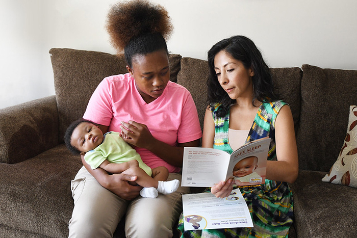Una nueva mamá con su bebé mira con otra mujer las recomendaciones de sueño infantil seguro.