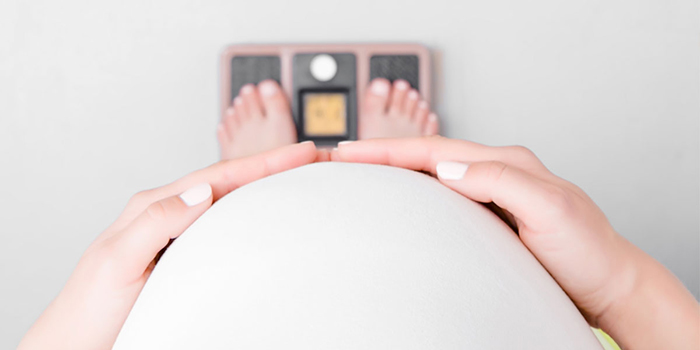 Mujer embarazada parada en una balanza con las manos sobre su vientre.