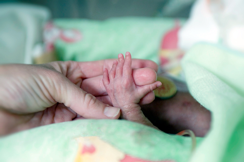 Una mano diminuta de un bebé prematuro toca el dedo de un adulto.