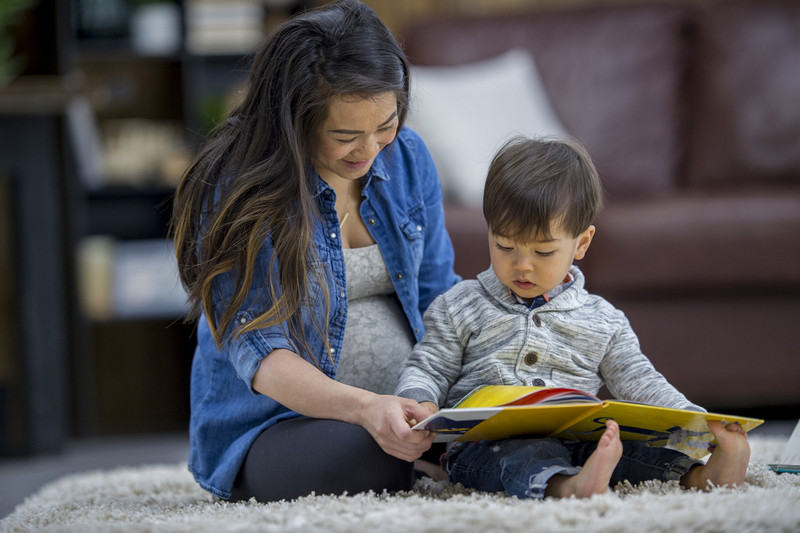 Mujer y niño sentados en una alfombra leyendo un libro juntos.