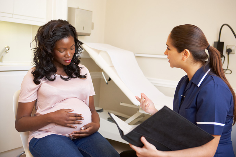 Una mujer afroamericana embarazada está con su médico que habla y sostiene una computadora portátil.
