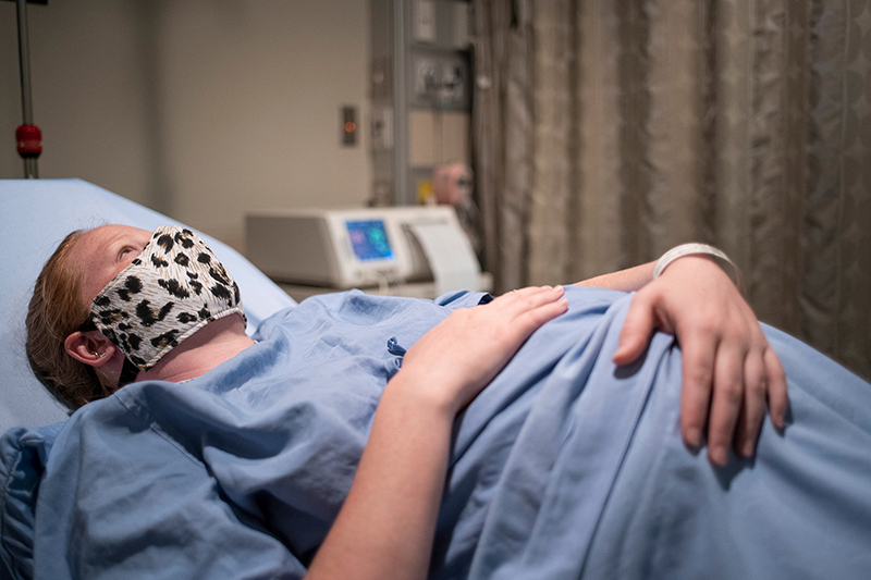 Mujer embarazada con mascarilla acostada en una cama de hospital.