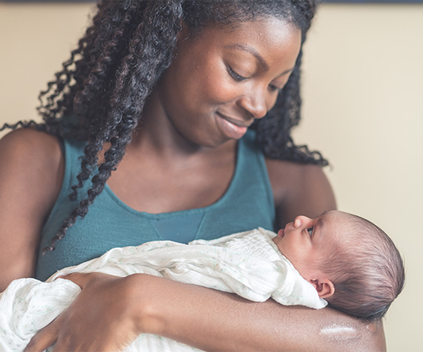 Una mujer afroamericana sonríe al bebé que sostiene en sus brazos.