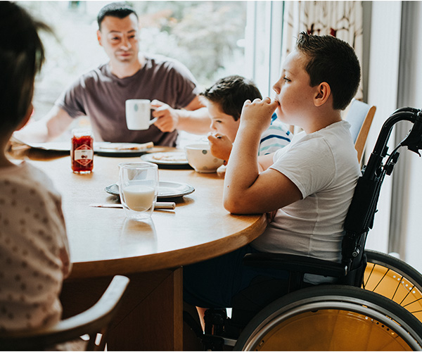 Un niño sentado en una silla de ruedas en una mesa come con su familia. 