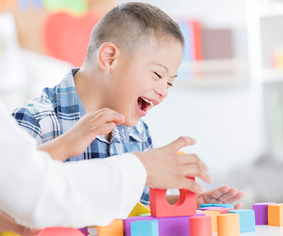 Un niño con síndrome de Down ríe mientras juega con bloques de construcción.