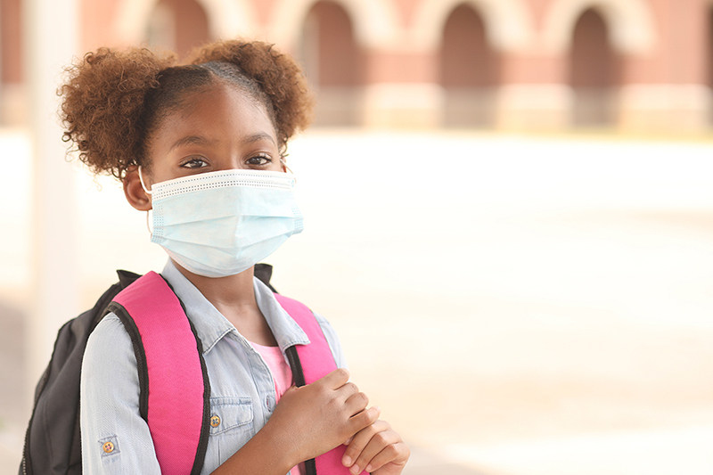 Niña negra/afroamericana en edad escolar primaria con mochila y máscara.