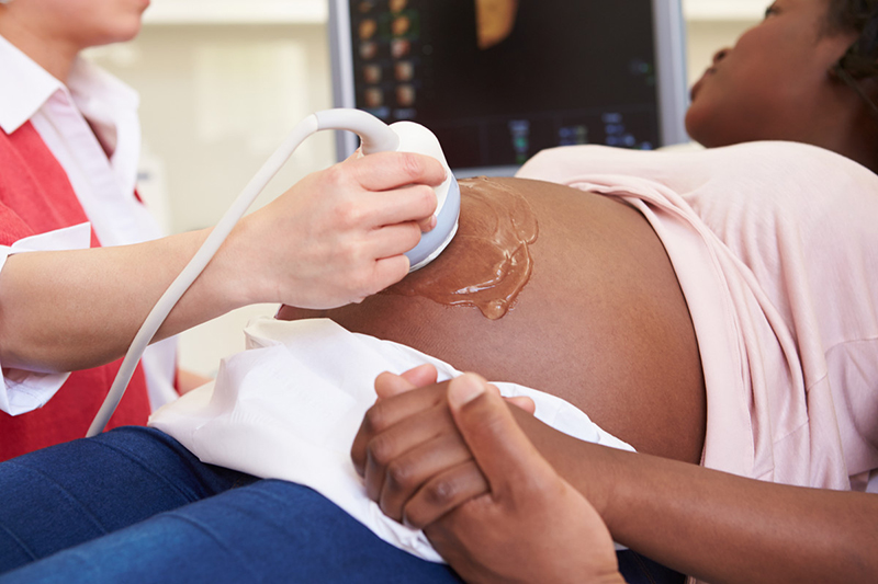Un técnico pasa un transductor de ultrasonido sobre el abdomen de una mujer embarazada.