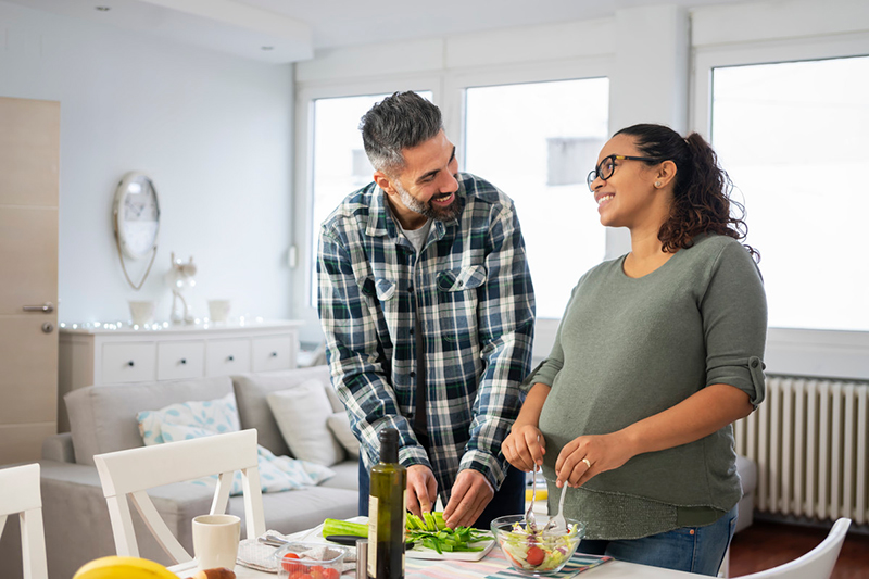 El hombre y la mujer embarazada de pie sobre la mesa preparando ensalada.
