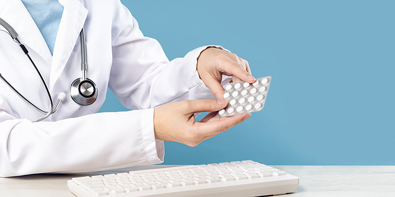 Manos que sostienen píldoras anticonceptivas hormonales sobre el teclado de una computadora.