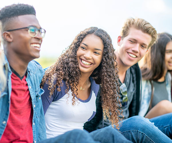 Grupo diverso de cinco adolescentes sentados al aire libre sonriendo.