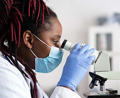 Una investigadora con mascarilla mira por un microscopio en un laboratorio.