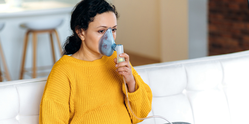 Persona embarazada sosteniendo un dispositivo de asistencia respiratoria en la cara.