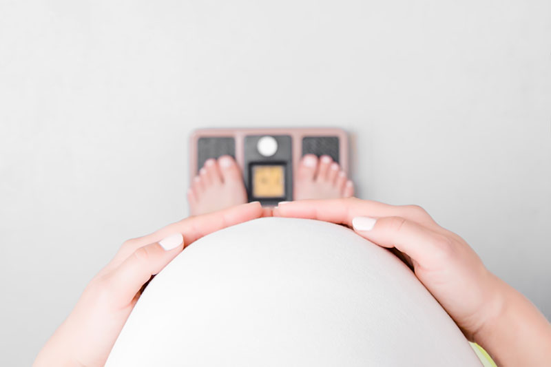Imagen desde el punto de vista de una mujer embarazada que mira sus pies en una balanza.