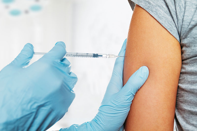 Manos con guantes que inyectan una vacuna en el brazo de una persona. 