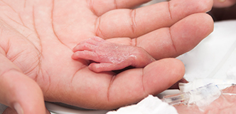 Mano adulta sosteniendo la mano de un pequeño bebé prematuro.
