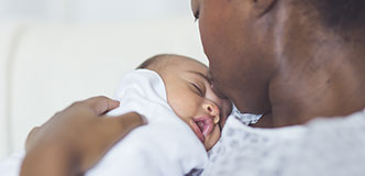 Una mujer negra con bata de hospital besa la frente de su bebé recién nacido.
