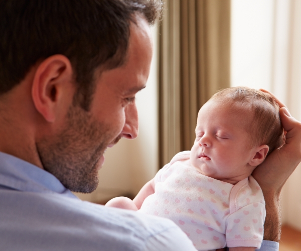 Un padre sonriente arrulla suavemente a un bebé recién nacido que duerme en sus manos.