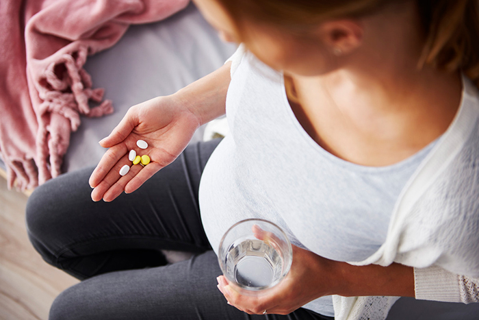 Una persona embarazada que sostiene tabletas de medicamentos en una mano y un vaso de agua en la otra.