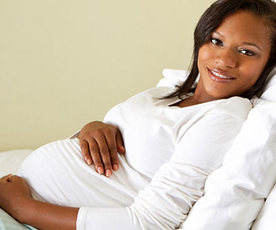 Una mujer embarazada sonriente sostiene su vientre mientras se recuesta en la cama