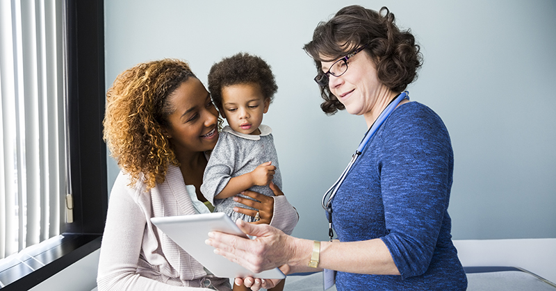 Un médico muestra una tableta digital a una madre con un niño en brazos.