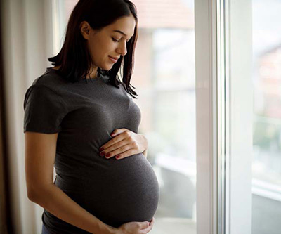 Una mujer embarazada con las manos en el abdomen se encuentra delante de una gran ventana.