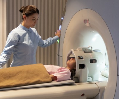 Un técnico de IRM observa a una joven que está recostada sobre un escáner de IRM.