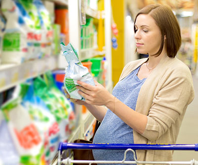 Una mujer embarazada se encuentra en el pasillo de una tienda examinando un paquete de detergente.
