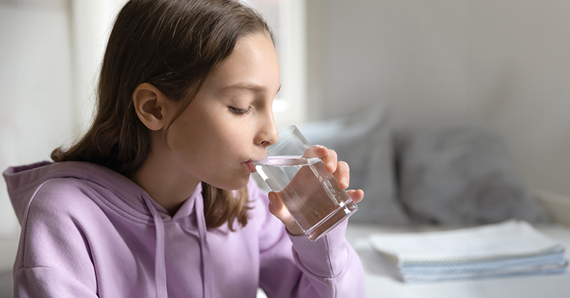 Una adolescente bebiendo un líquido transparente de un vaso transparente.