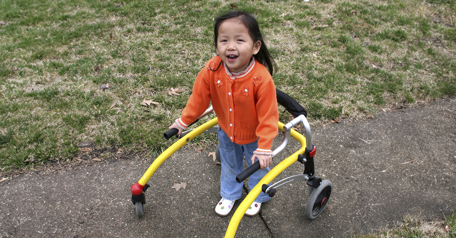 Niño de pie, sujetando los rieles de un andador asistido.