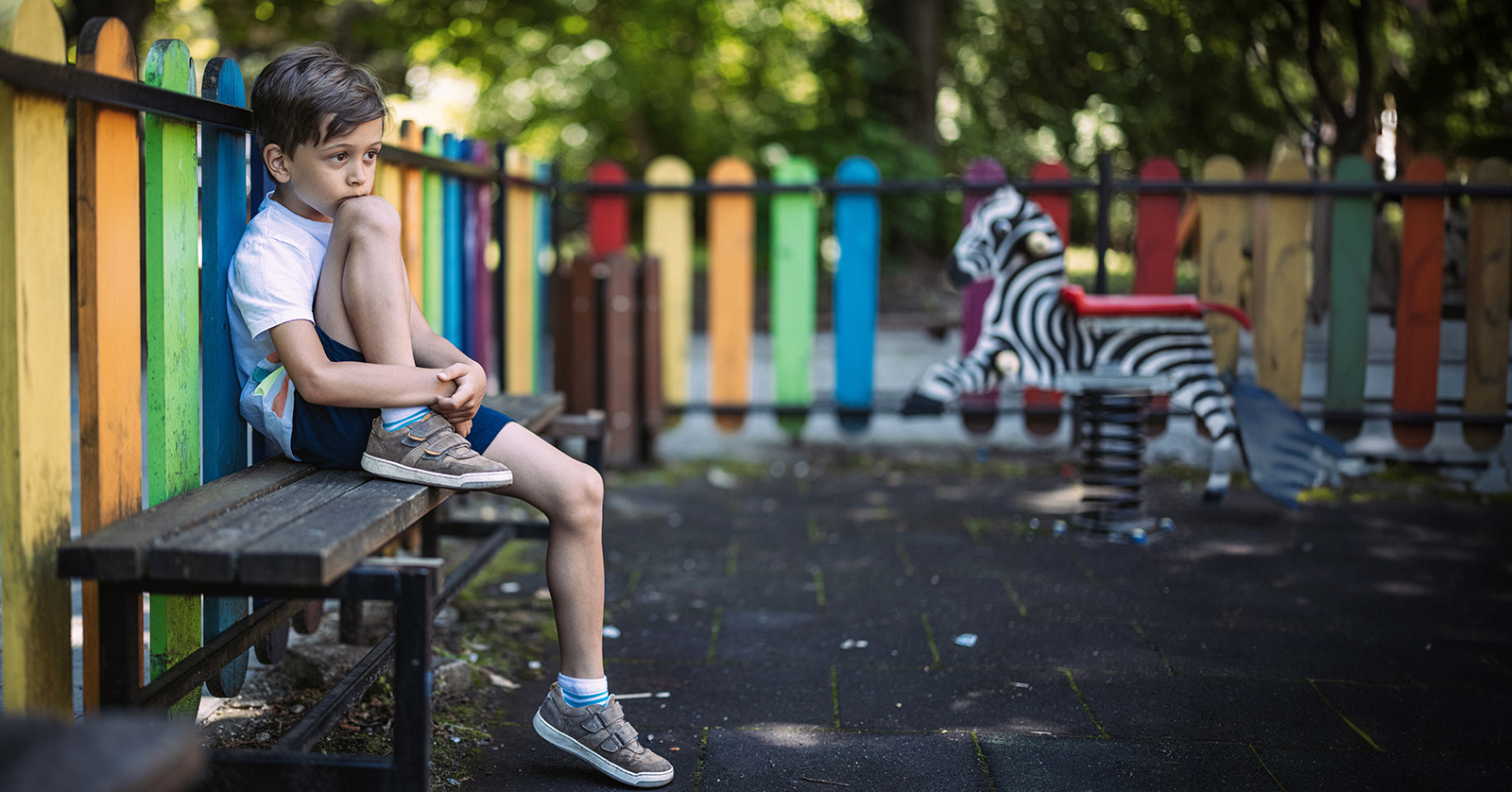 Un niño sentado solo en un banco del parque infantil.