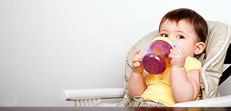 Niño pequeño en una silla alta para bebés bebiendo jugo de un vaso con pajita.