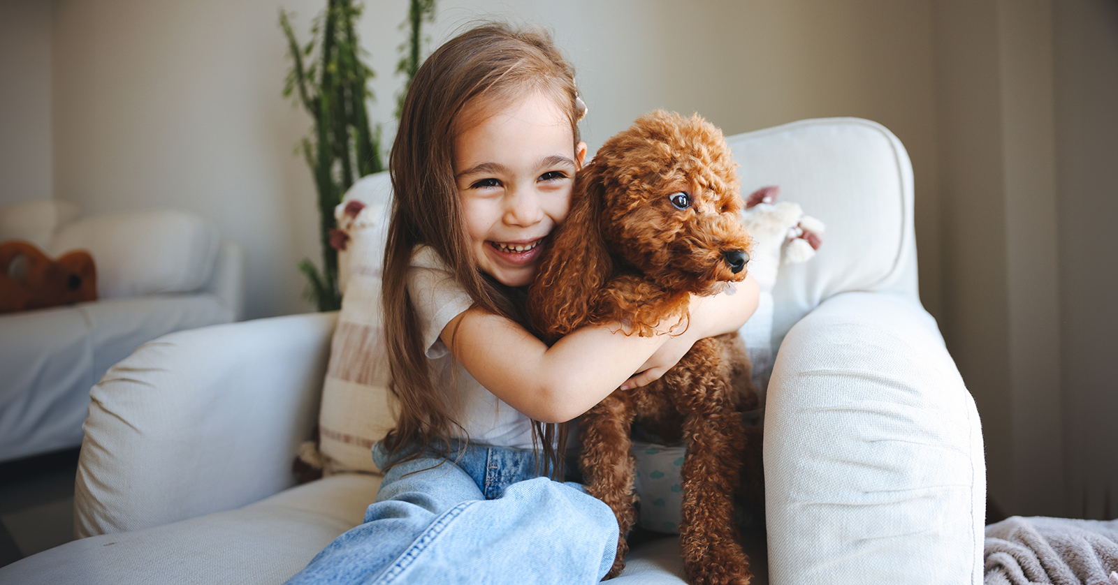 Una niña sonríe mientras abraza a un perro pequeño.