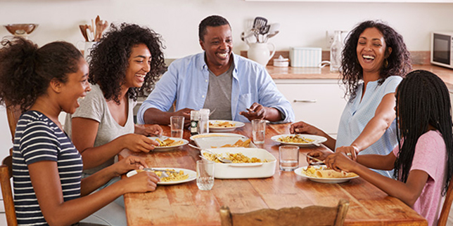 Los padres y sus tres hijos sentados a la mesa de la cocina comen juntos.