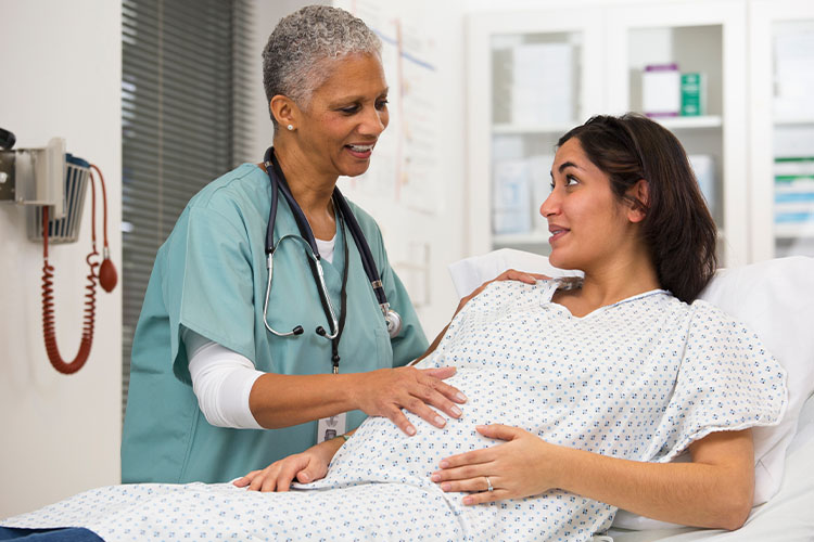 Una mujer embarazada está sentada en una cama de hospital y habla con un profesional de la salud.