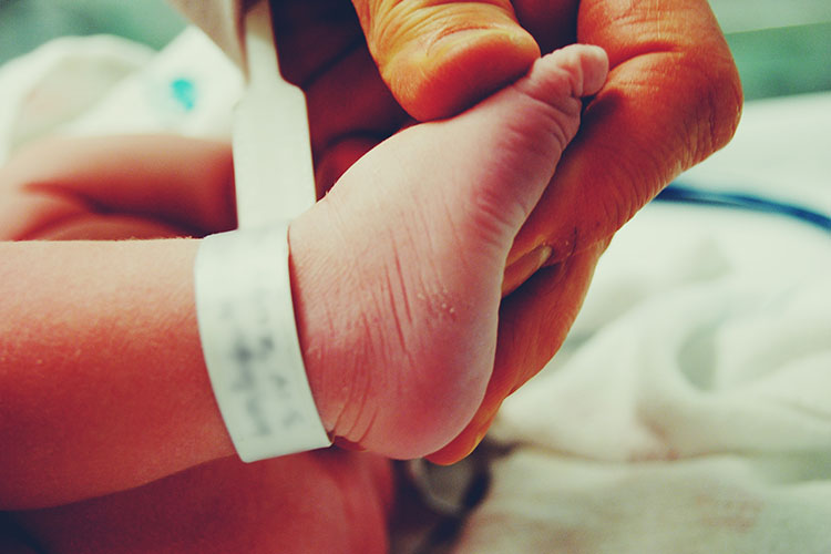 El pie de un recién nacido, con una etiqueta hospitalaria en el tobillo, lo sujeta una mano adulta.