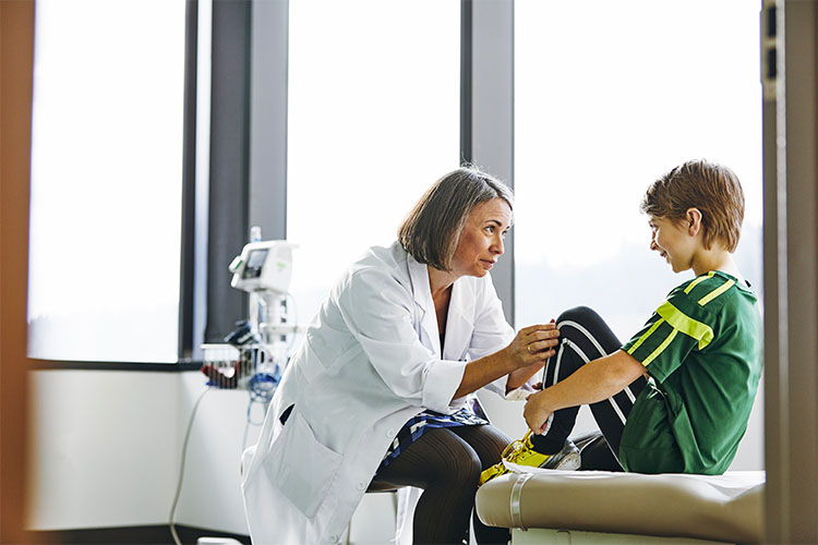 Una persona joven está sentada con los brazos alrededor de las rodillas dobladas, delante de un profesional de la salud.