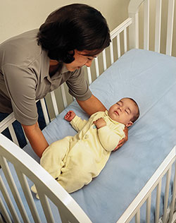 Imagen de una madre que acuesta a su bebé a dormir boca arriba en la cuna.